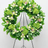 Green floral wreath with orchids and roses displayed on a black metal easel