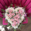 A heart-shaped floral arrangement of blush pink roses layered over creamy white