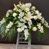 White floral funeral spray with lilies and roses on a stand