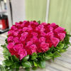 Heart-shaped arrangement of pink and red roses edged with glossy green foliage on a wooden surface