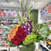 Tall arrangement of red roses, calla lilies, orchids and green hydrangea in a round glass vase with large tropical leaves.