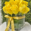 Compact arrangement of bright yellow roses in a clear cube vase with a yellow ribbon bow