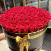 Large round hat box filled with tightly packed red roses and tied with a gold ribbon.