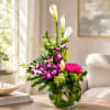 Tall floral arrangement with white calla lilies, purple orchids, and pink roses in a glass vase.