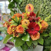 Fall arrangement of orange roses and red gerbera daisies in a round glass vase with a turkey pick