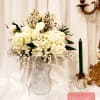 White floral arrangement in a tall vase beside a green candle