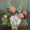 A garden inspired arrangement featuring soft blue hydrangea, peach roses, and delicate