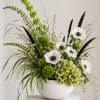 Green and white floral arrangement in a white bowl vase