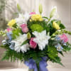 Bouquet of white lilies, pink roses, and yellow carnations in a vase with a purple ribbon
