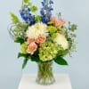 Mixed bouquet in a clear glass vase with blue, peach, and white blooms