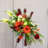 Tall mixed floral arrangement with orange gerberas and red blooms on a stand