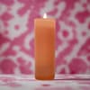 Lit orange pillar candle against a pink patterned background