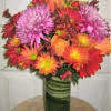 Colorful bouquet of pink, orange, and red flowers in a green glass vase