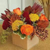 Orange and burgundy floral arrangement in a square box