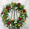 Large floral wreath with red roses, sunflowers, and green mums on an easel