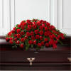 Red rose and carnation casket spray with ribbon on a dark wood casket