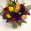 Mixed bouquet of purple, yellow, and peach flowers in a glass vase