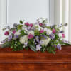 Casket spray with pink roses, white flowers, and purple accents