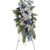 Standing floral spray with white lilies, roses, and blue flowers on an easel