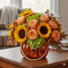 Low centerpiece of yellow sunflowers, peach roses, and green hydrangea in an orange pumpkin-shaped vase.