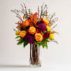 Orange and yellow roses with purple blooms in a clear glass vase