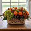 Low fall centerpiece with orange roses, orchids, and green hydrangeas in a rectangular ceramic container