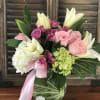 Pink and white lilies, roses, and hydrangeas in a clear glass vase with a pink ribbon bow