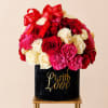 Red, pink, and cream roses arranged in a black box with red ribbons