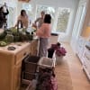 People arranging purple flowers and greenery on a kitchen island