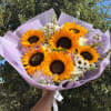 Handheld bouquet of sunflowers and pastel mixed flowers wrapped in lavender paper