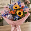 Bouquet of sunflowers, orange roses, and blue flowers wrapped in pink paper