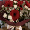 Bouquet of red gerbera daisies and white carnations wrapped in burgundy paper