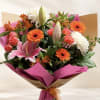 Bouquet of pink lilies, orange gerberas, roses, and white chrysanthemums wrapped in pink paper