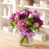 Mixed pink and purple bouquet in a clear square vase with a lavender ribbon