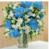 Blue hydrangeas and white lilies in a clear glass vase