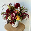 Autumn floral arrangement with burgundy blooms, orchids, and small pumpkins in a white vase