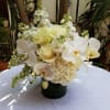 White floral arrangement in a dark vase with orchids and roses