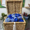 Blue roses and hydrangeas arranged in a woven basket with a white ribbon