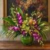Purple and green orchid arrangement in a round glass vase