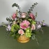 Pink gerbera daisies and roses in a woven basket with lavender accents