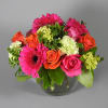 Mixed bouquet of pink gerberas, roses, and orange blooms in a glass vase