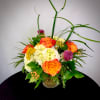 Orange roses and white hydrangeas in a glass vase with tall grass accents