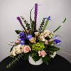 Mixed bouquet with pink roses, blue irises, and purple spikes in a white vase