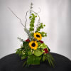 Tall floral arrangement with sunflowers and red roses in a low container
