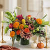 Colorful autumn floral arrangement in a green vase with pumpkins nearby