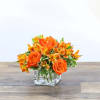 A clear cube holds orange roses and orange alstroemeria. Simple and bright.