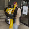 Person holding a large bouquet of white roses and yellow sunflowers wrapped in black paper