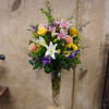 Mixed bouquet of lilies, roses, and purple flowers in a tall glass vase