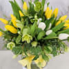 Yellow and white tulip arrangement with green blooms in a round vase with ivy and a yellow ribbon bow.