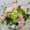 Round arrangement of pale pink roses and green hydrangeas in a clear glass vase